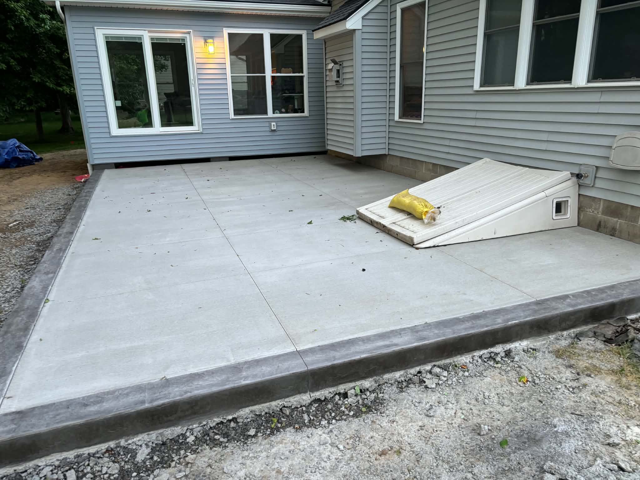 Broom-finish concrete patio wrapping a basement cellar entry with hand-troweled picture-frame border in Webster NY