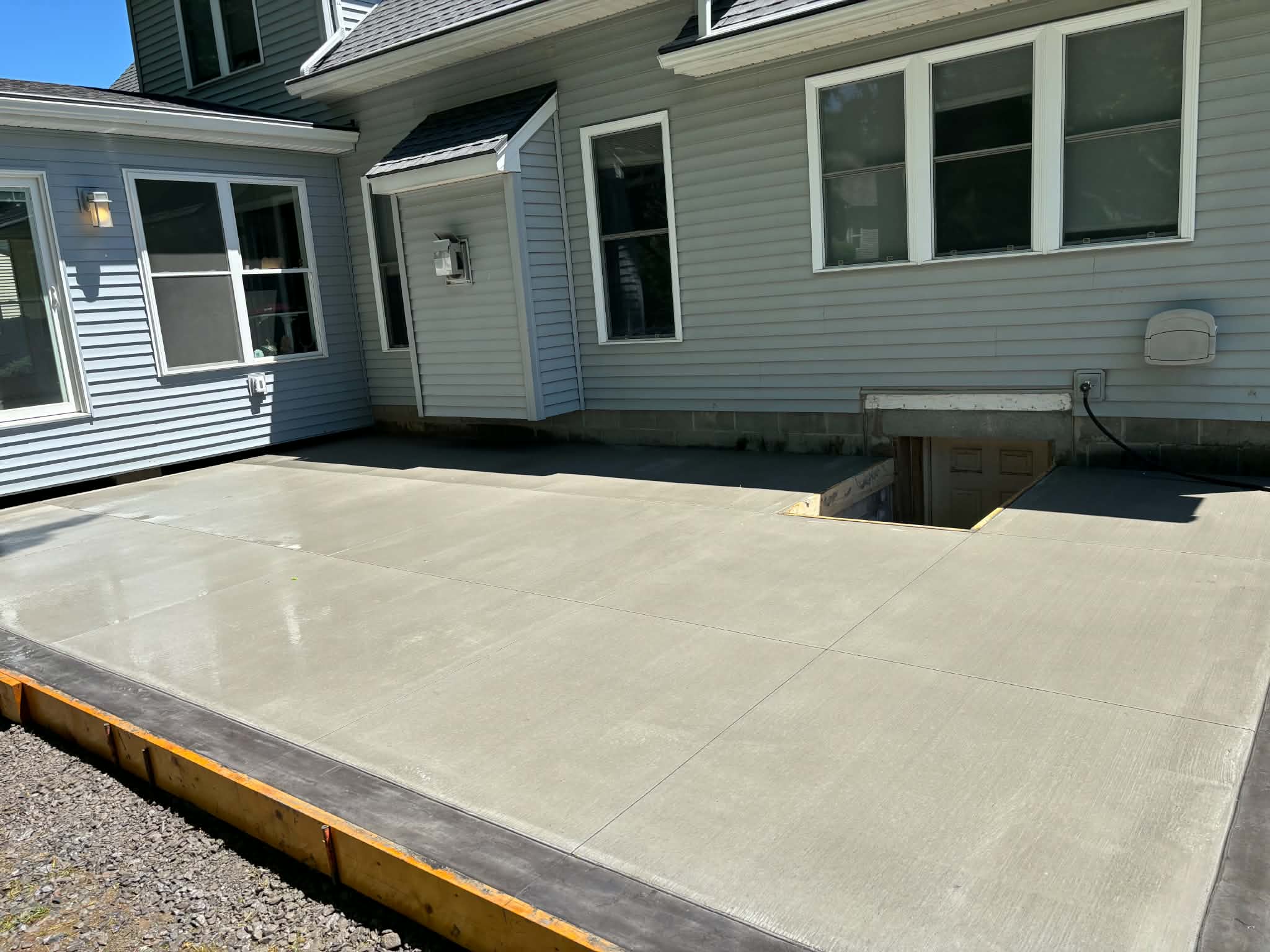 Large-scale concrete patio with picture-frame border wrapping a cellar entry in Webster NY